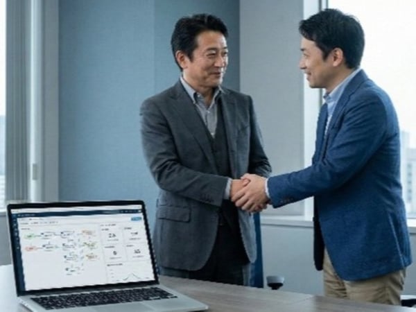 経営者とシステムコンサルタントが、PC画面を見ながら笑顔で握手をしている写真